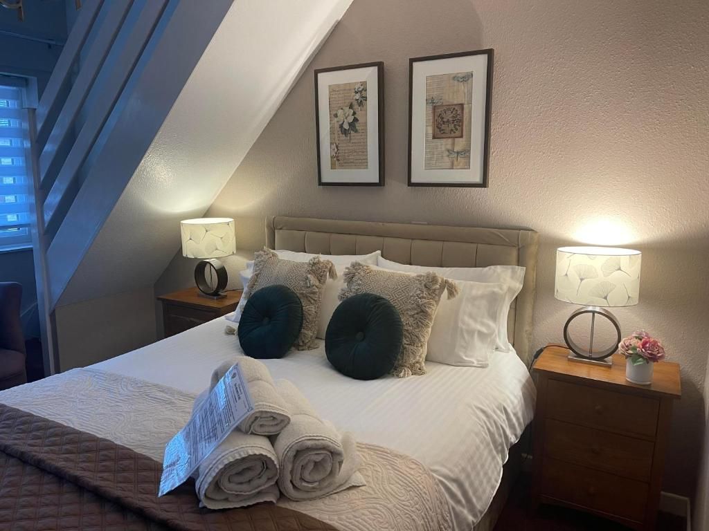 A neatly made bed with rolled towels, two bedside lamps, and framed artwork on the wall.