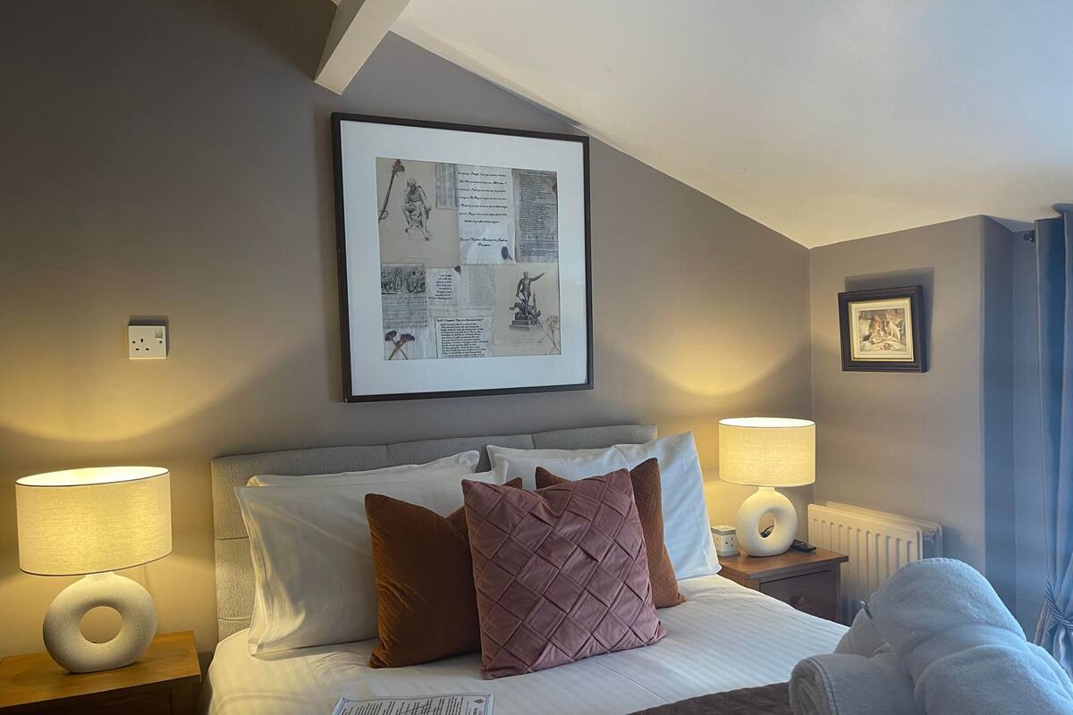 A hotel room with a neatly made bed, two bedside lamps, a framed artwork above the bed, and a framed picture on the wall.