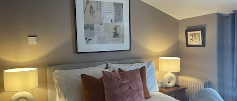 Habitació d'hotel amb un llit ben fet, dues làmpades al costat del llit, una obra d'art emmarcada sobre el llit i una fotografia penjada a la paret.