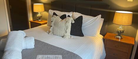A neatly made bed with a patterned bedspread, two bedside lamps, a nightstand with a lamp, and two framed pictures on the wall.