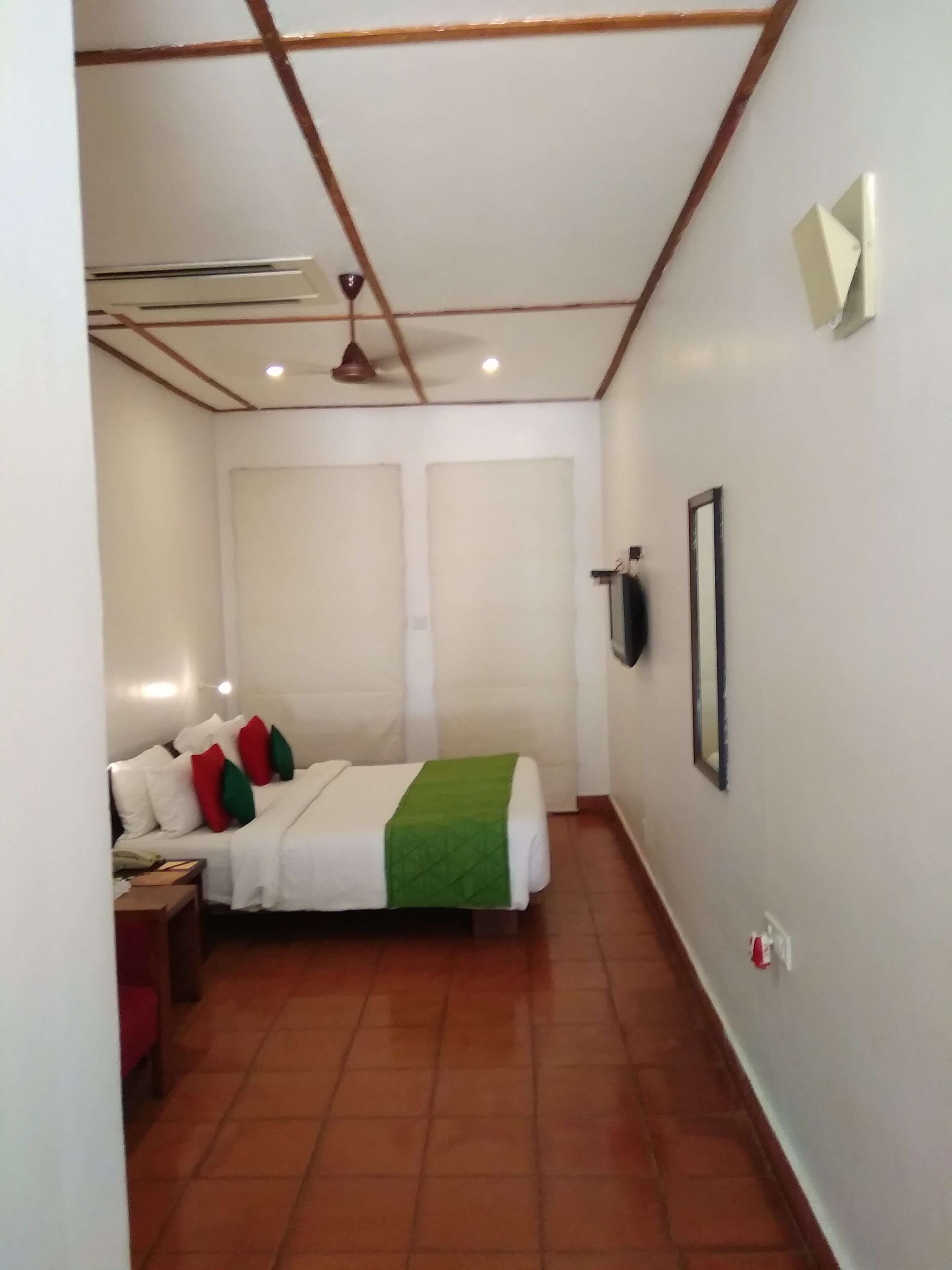 Un dormitori amb llit, ventilador al sostre, televisió penjada i una llum de senyalització vermella.