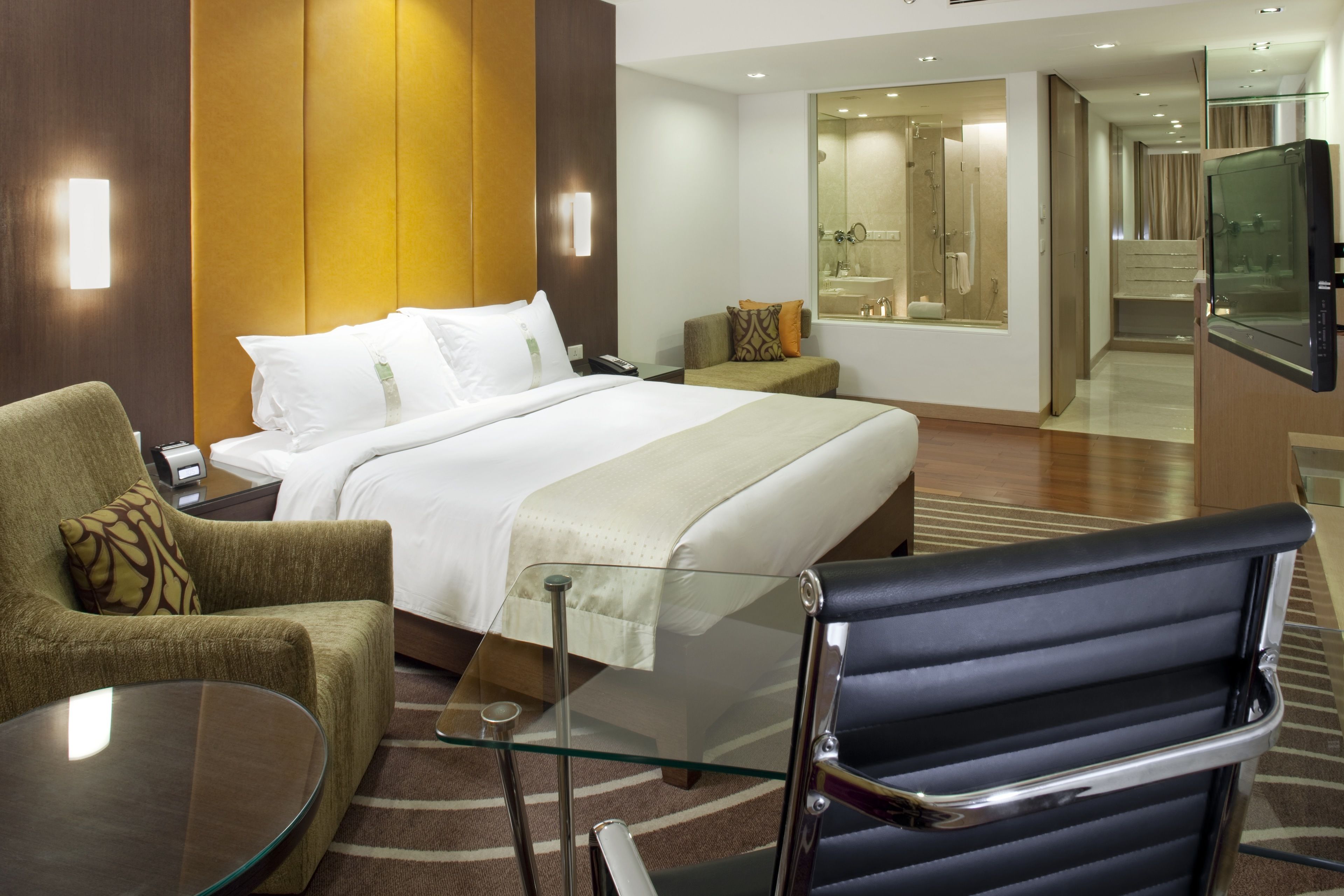A hotel room with a bed, a sitting area with a glass table, a sofa, and a TV.