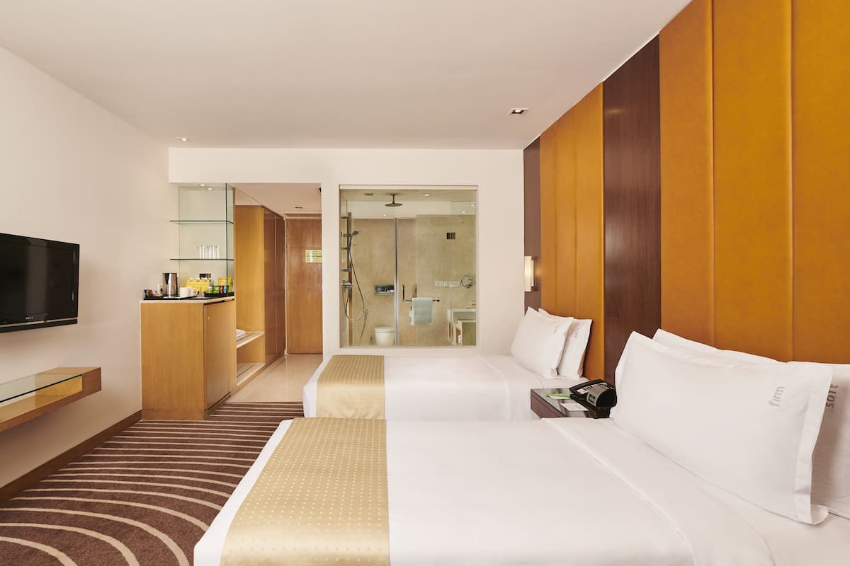 A hotel room with two beds, a TV, a minibar, and a bathroom visible through an open door.