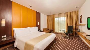 A hotel room with a large bed, a desk with a chair, a television, and a window with curtains.