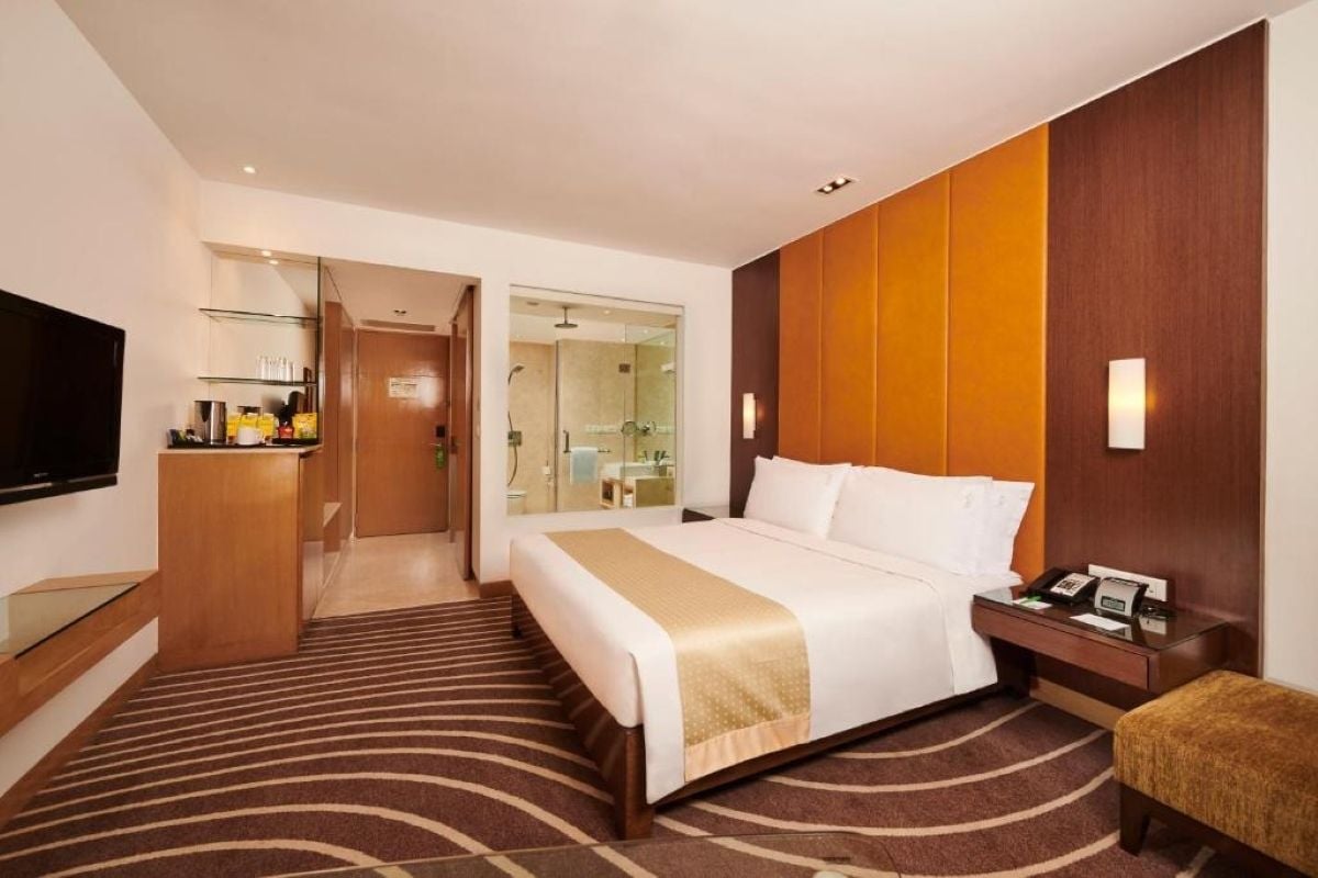 Een hotelkamer met een bed, nachtkastje, televisie en een badkamer, zichtbaar door een geopende deur.