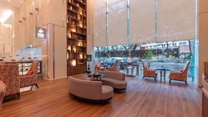 A modern interior with a curved sofa, armchairs, a coffee table, and a large window offering a view of the street.