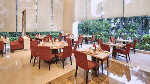 A spacious restaurant with red upholstered chairs and tables, large windows offering a view of greenery outside.