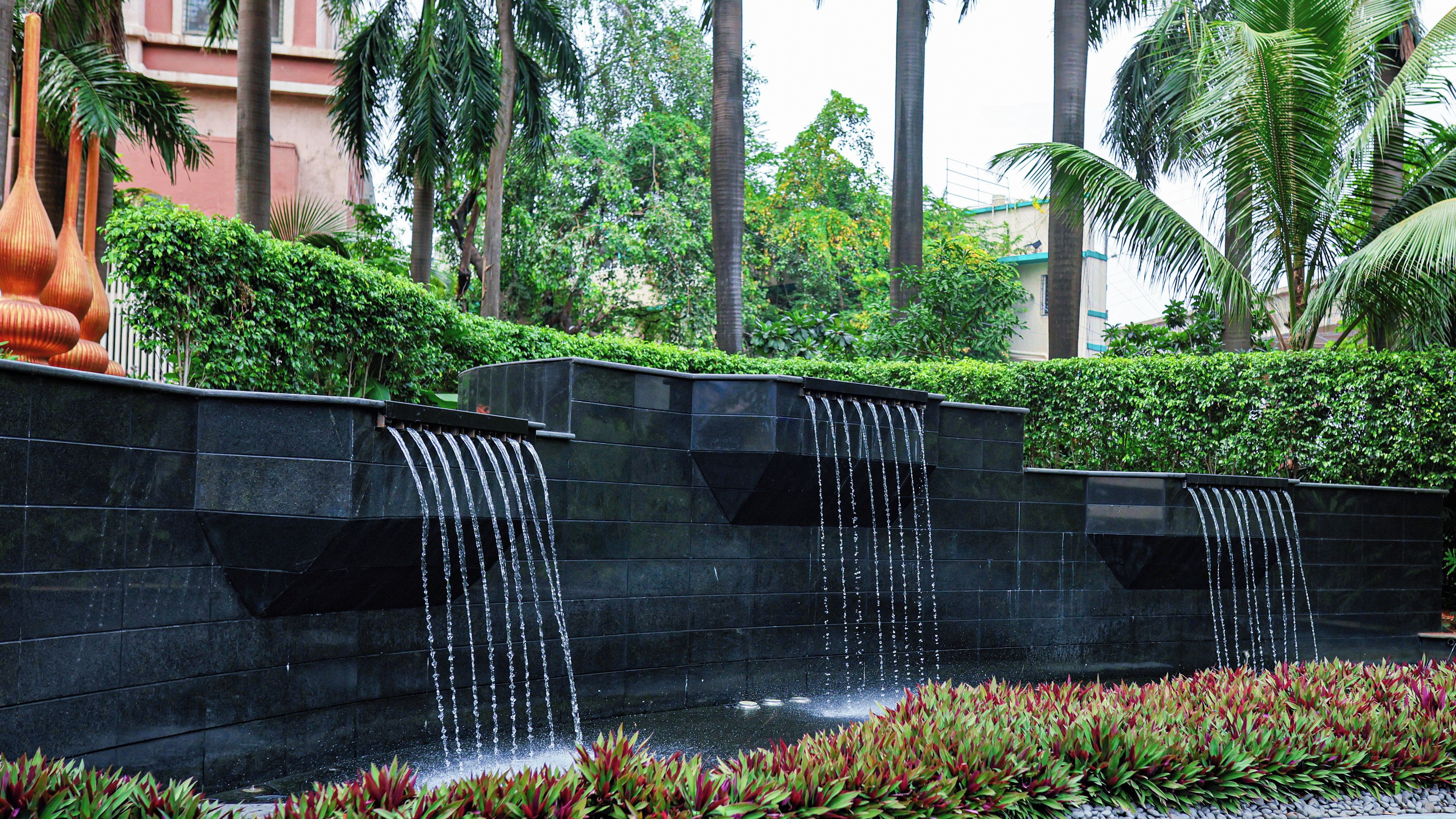A water feature with multiple cascades, surrounded by greenery and palm trees.