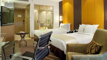 Une chambre d’hôtel avec un lit, une chaise, un bureau et une salle de bain visible à travers une porte ouverte.