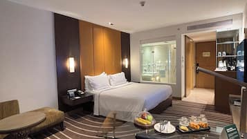 A hotel room with a bed, a desk with a chair, a small table with a glass top, and a sofa.