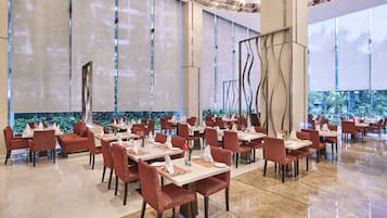 A spacious restaurant with high ceilings, modern decor, and large windows offering a view of greenery.