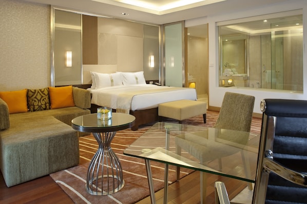 A modern hotel room with a bed, sofa, armchair, and a glass table.