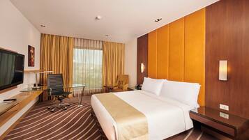 A hotel room with a large bed, a desk with a computer, a chair, a television, and a window with curtains.