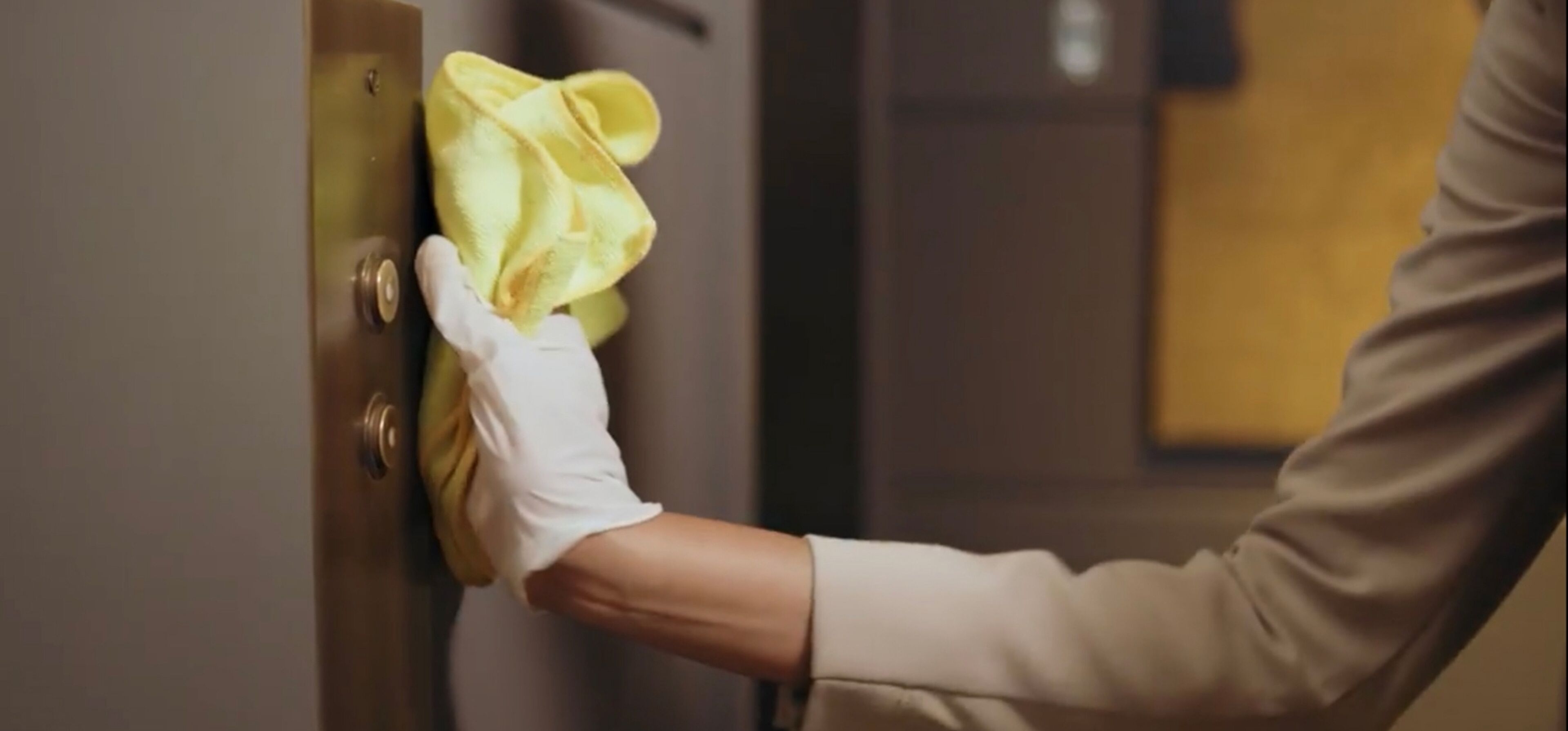 A person cleaning a door handle with a yellow cloth.