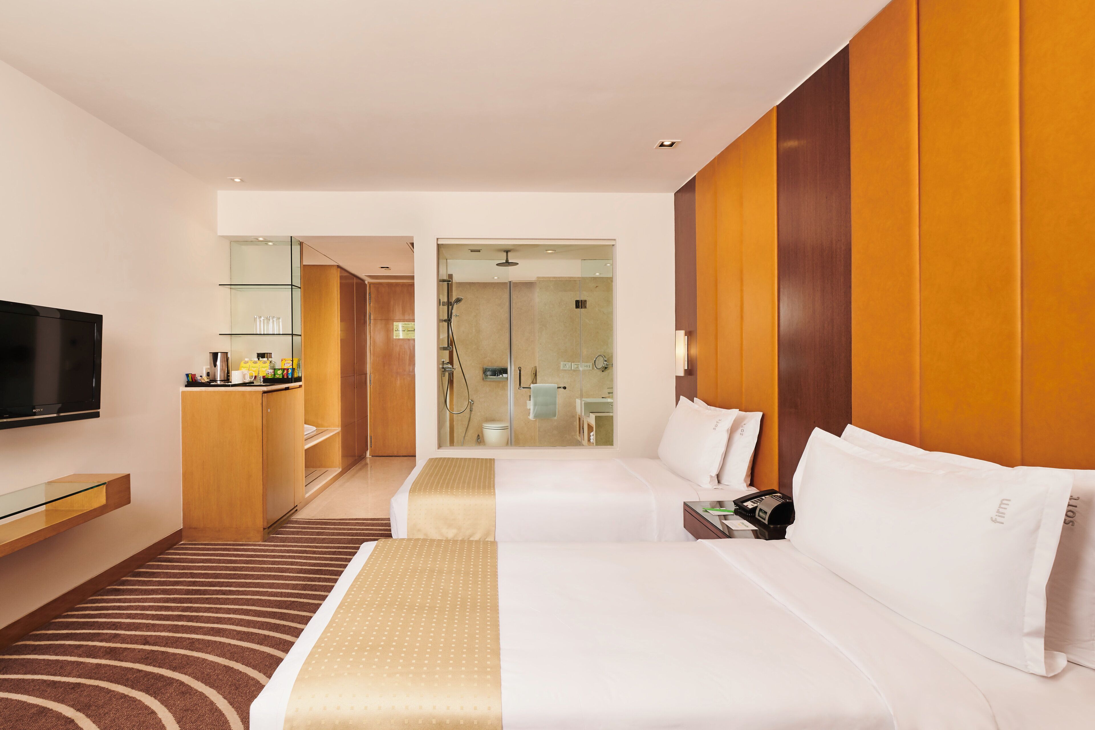 A hotel room with a bed, bedside table, TV, and a bathroom visible through a glass door.