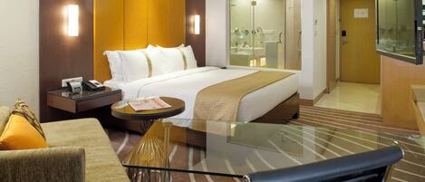 A hotel room with a bed, bedside table, chair, and a glass table.