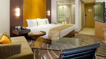 A hotel room with a bed, a glass table, a sofa, and a chair.