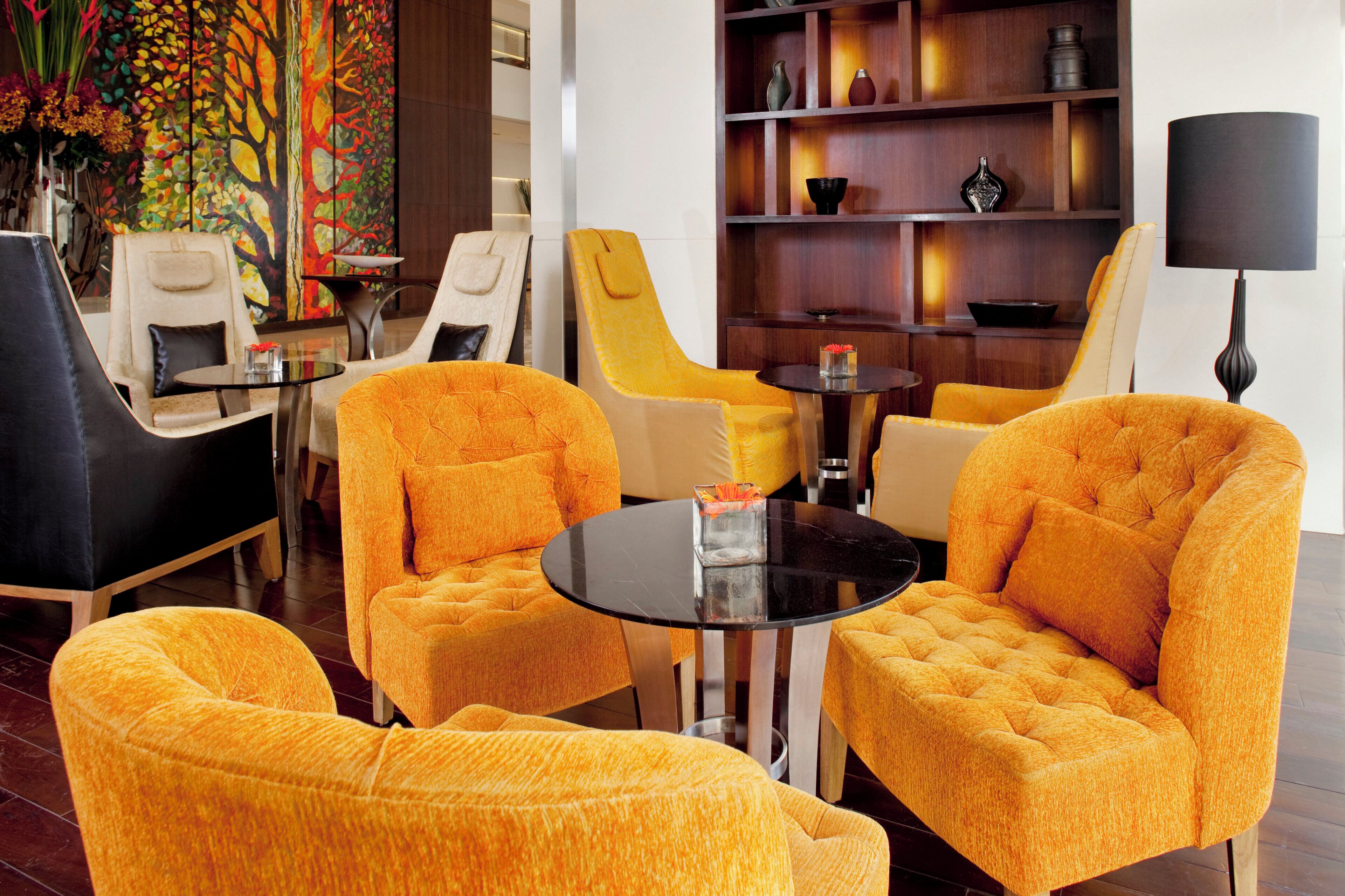 A hotel lobby with yellow upholstered chairs, a black round table, and a wooden bookshelf with decorative items.