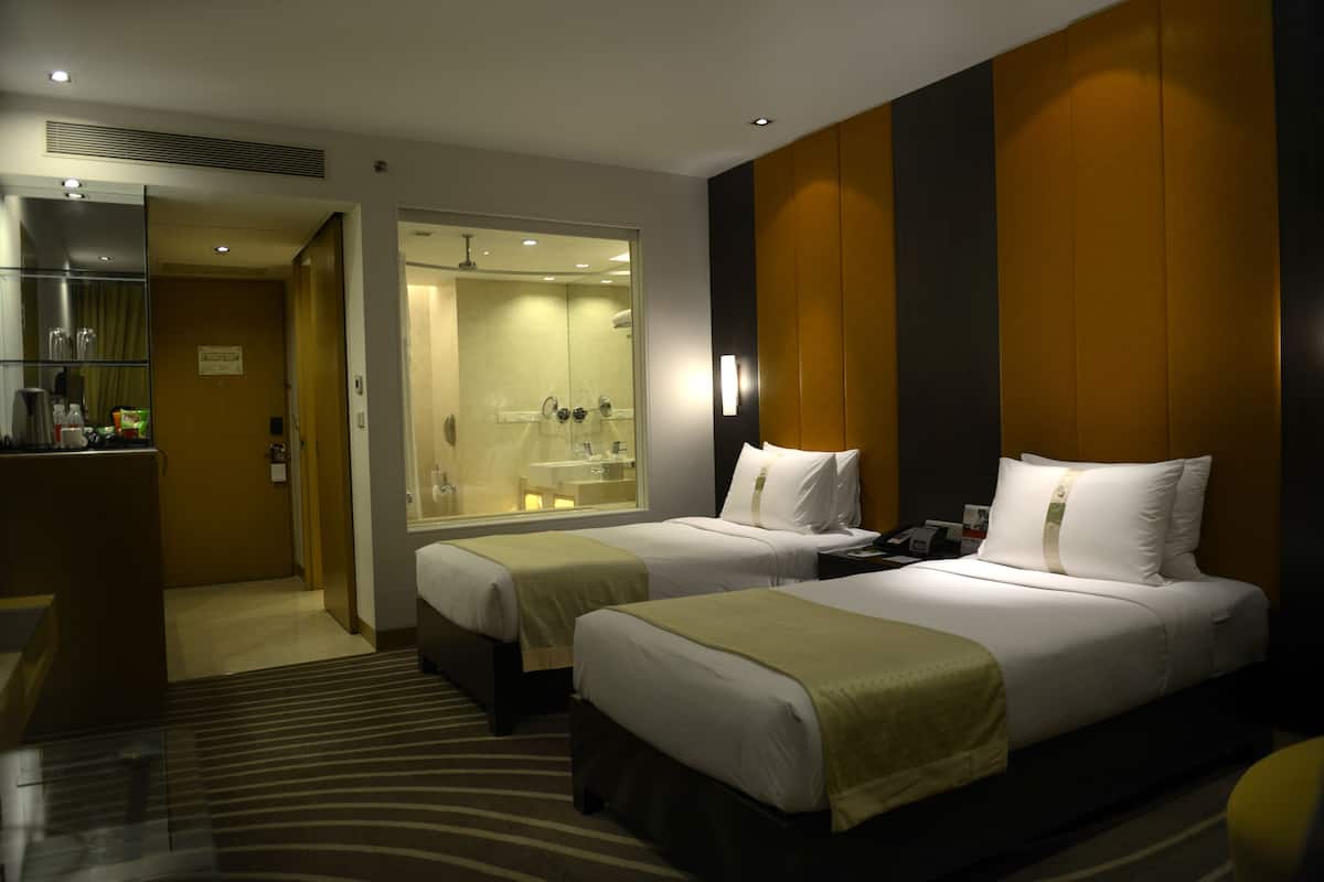 A hotel room with two beds, a bathroom, and a desk with a mirror.