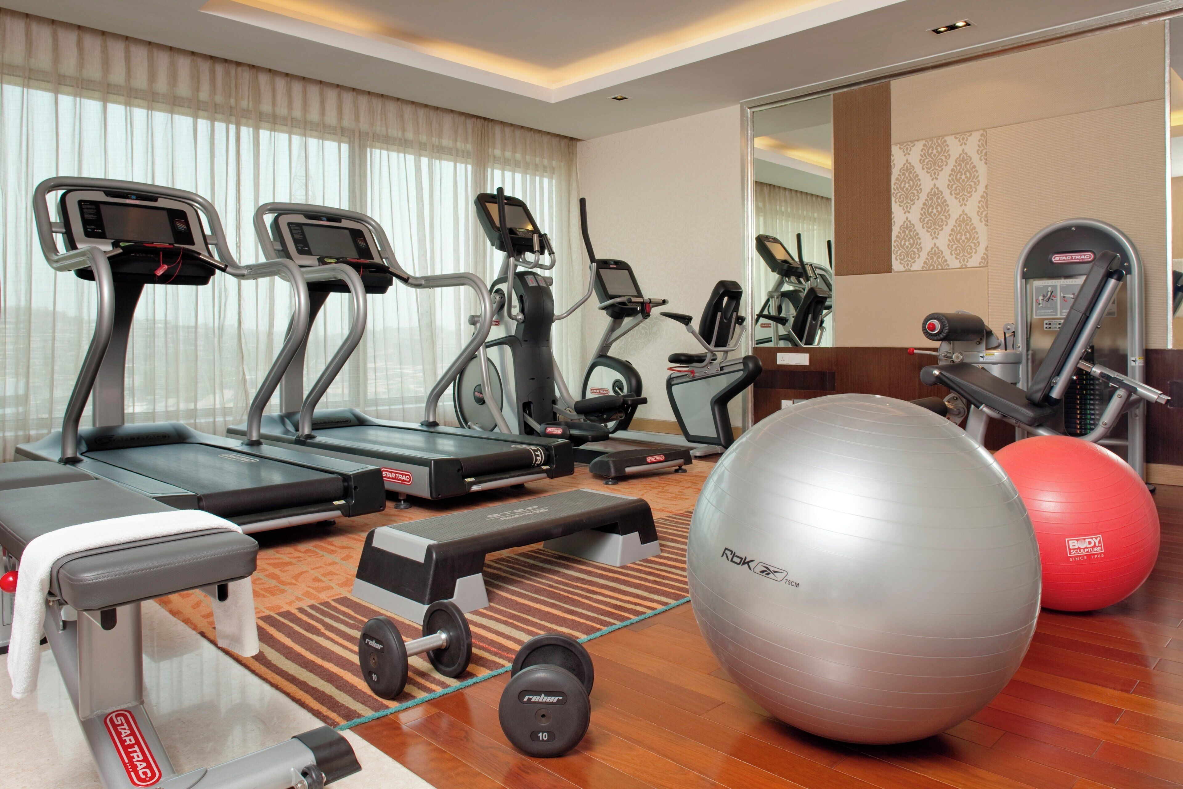 A hotel fitness center with treadmills, elliptical machines, a rowing machine, free weights, and exercise balls.