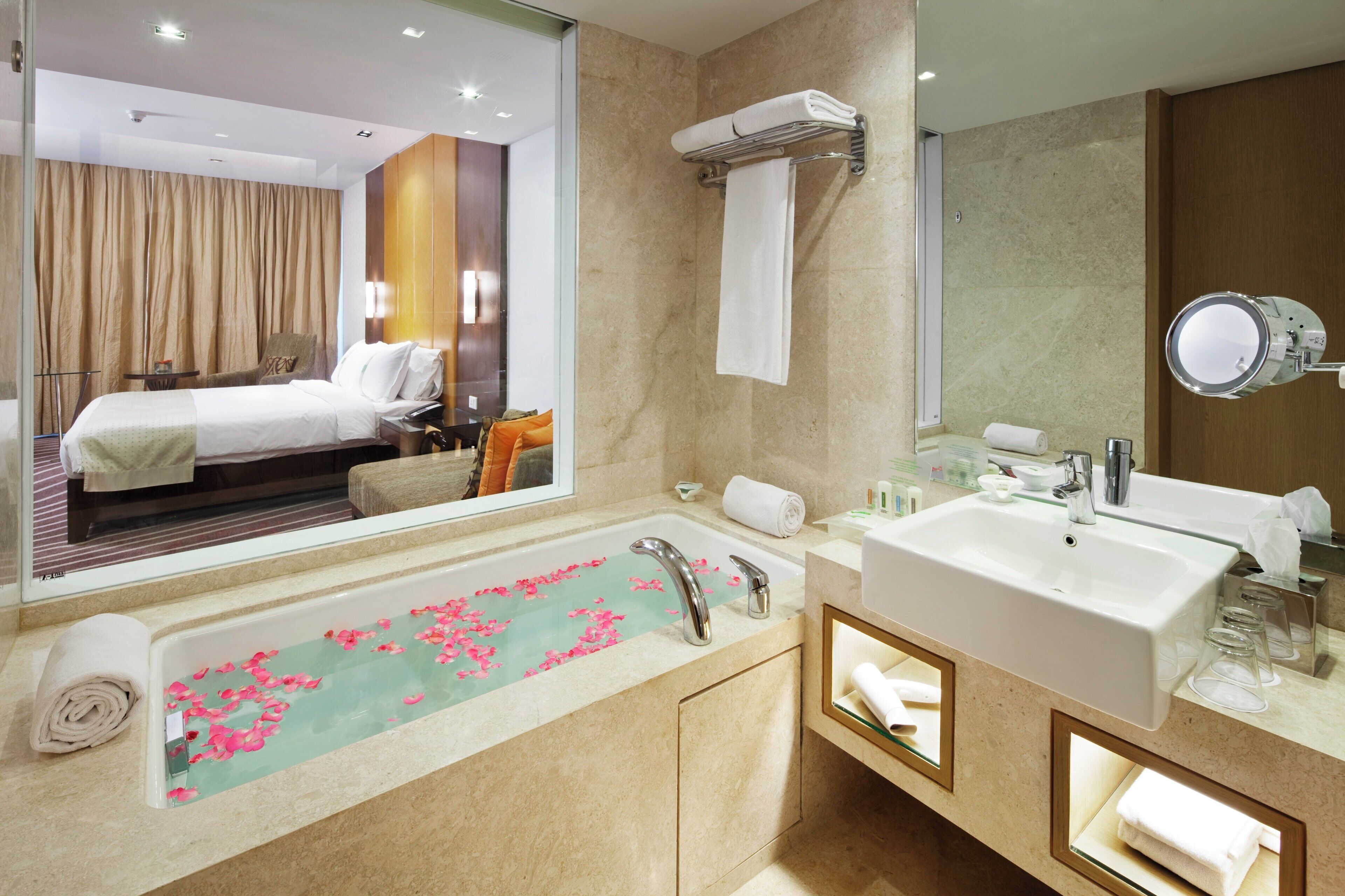 A hotel bathroom with a large bathtub, a sink, a mirror, and a towel rack.