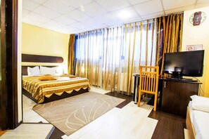 Una camera d'albergo con un letto, una scrivania, un televisore e tende.