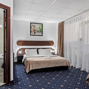 Una habitación de hotel con cama, un cuadro, una ventana con cortinas y una alfombra estampada.