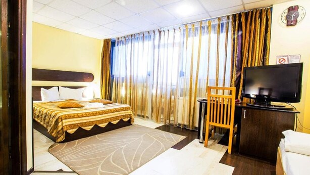 A hotel room with a bed, a desk, a television, and curtains. - Charter Otopeni (Otopeni)