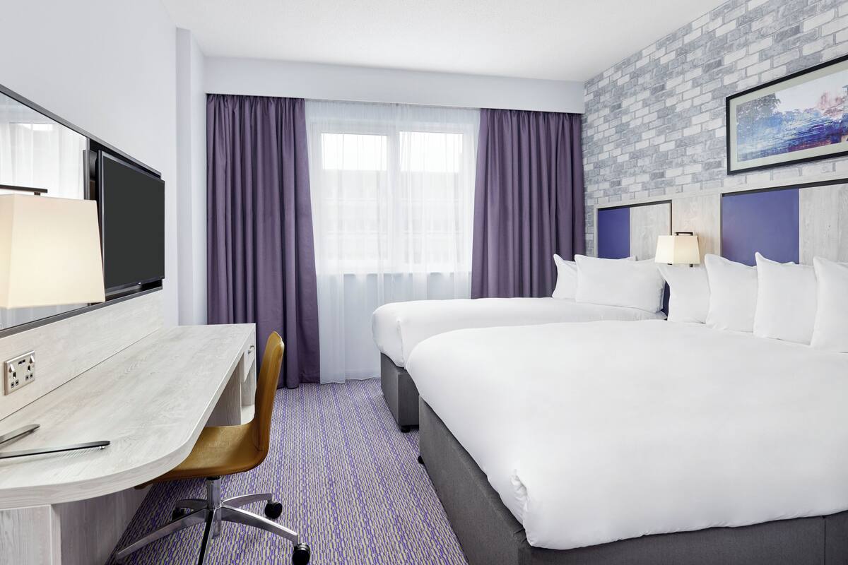 A hotel room with a bed, a desk, a chair, a TV, and a window with curtains.