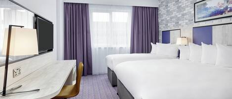 A hotel room with a bed, a desk, a chair, a TV, and a window with curtains.