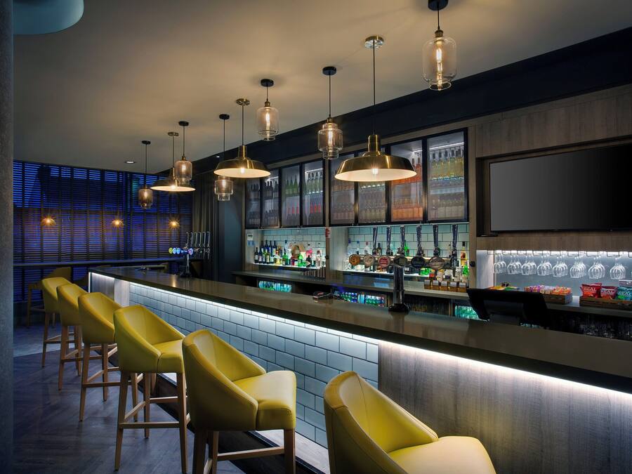 A bar area with multiple stools, a bar counter, and a variety of bottles and glasses.