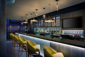 A bar area with multiple stools, a bar counter, and a variety of bottles and glasses.