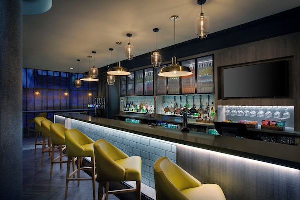 A bar area with multiple stools, a bar counter, and a variety of bottles and glasses. - Leonardo Hotel Swindon (Swindon)