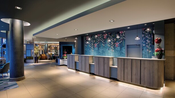 A modern hotel lobby with a reception desk, seating area, and a large wall mural.