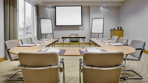 A conference room with a large table, chairs, a projector screen, whiteboards, and a cabinet with a coffee machine.