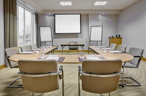 A conference room with a large table, chairs, a projector screen, whiteboards, and a cabinet with a coffee machine. - Leonardo Hotel Swindon  (Swindon)