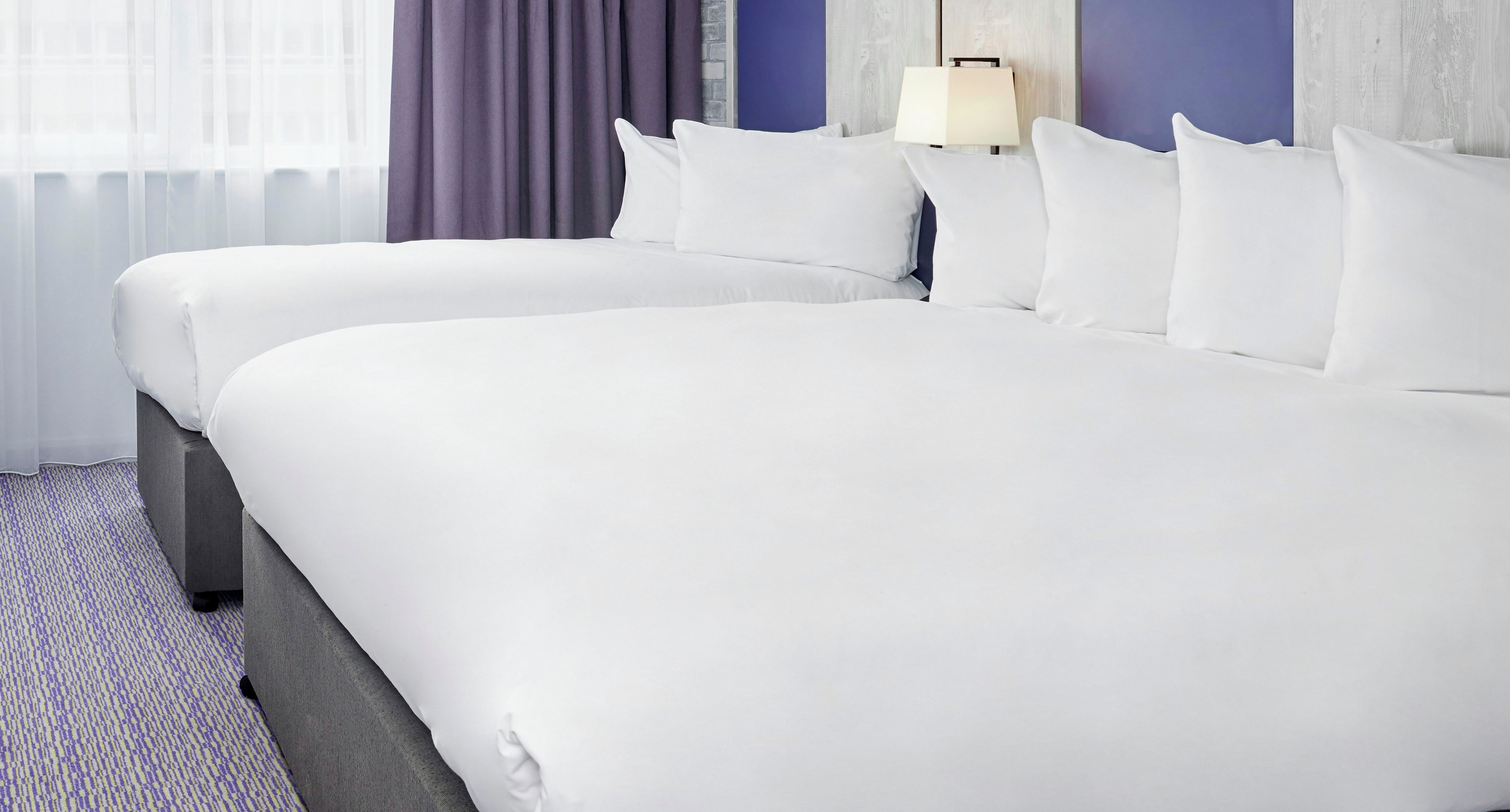 A hotel room with two beds, a lamp, and a window with curtains.