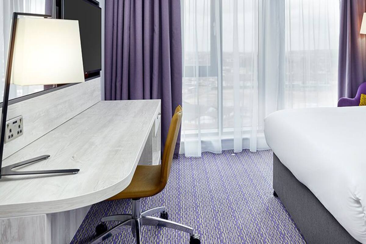 A hotel room with a bed, a desk, a chair, and a window with curtains.