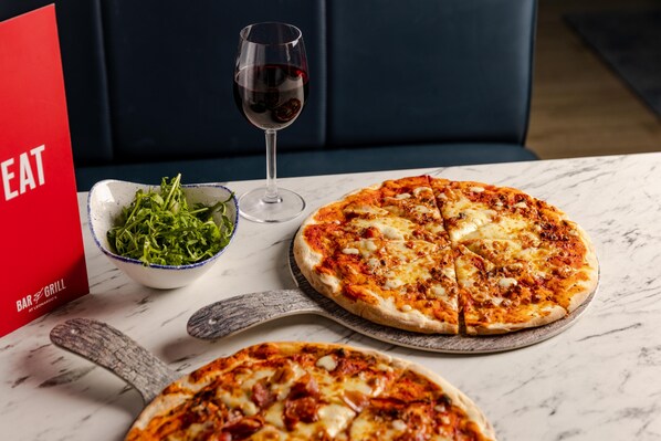 A pizza with a glass of red wine and a bowl of greens on a table.