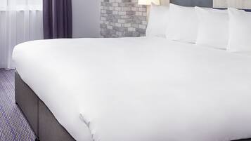 A large bed with white linens, a headboard with a blue accent, and a brick-patterned wall behind it.