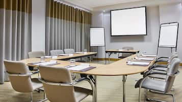 A conference room with a long table, multiple chairs, a projector screen, and a whiteboard.