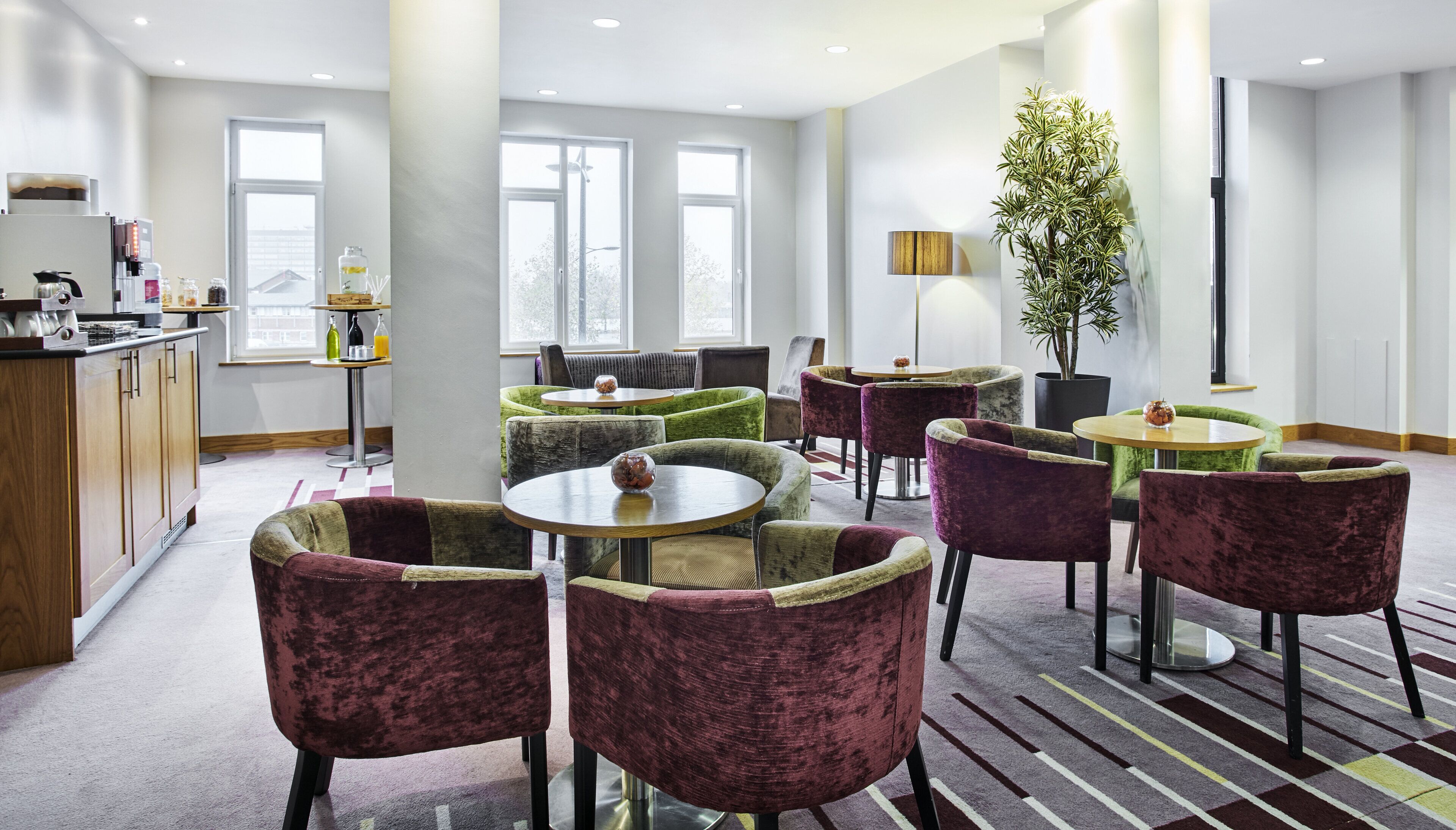 Un hall d’hôtel aménagé avec des espaces salon, un coin café et une grande plante en pot.