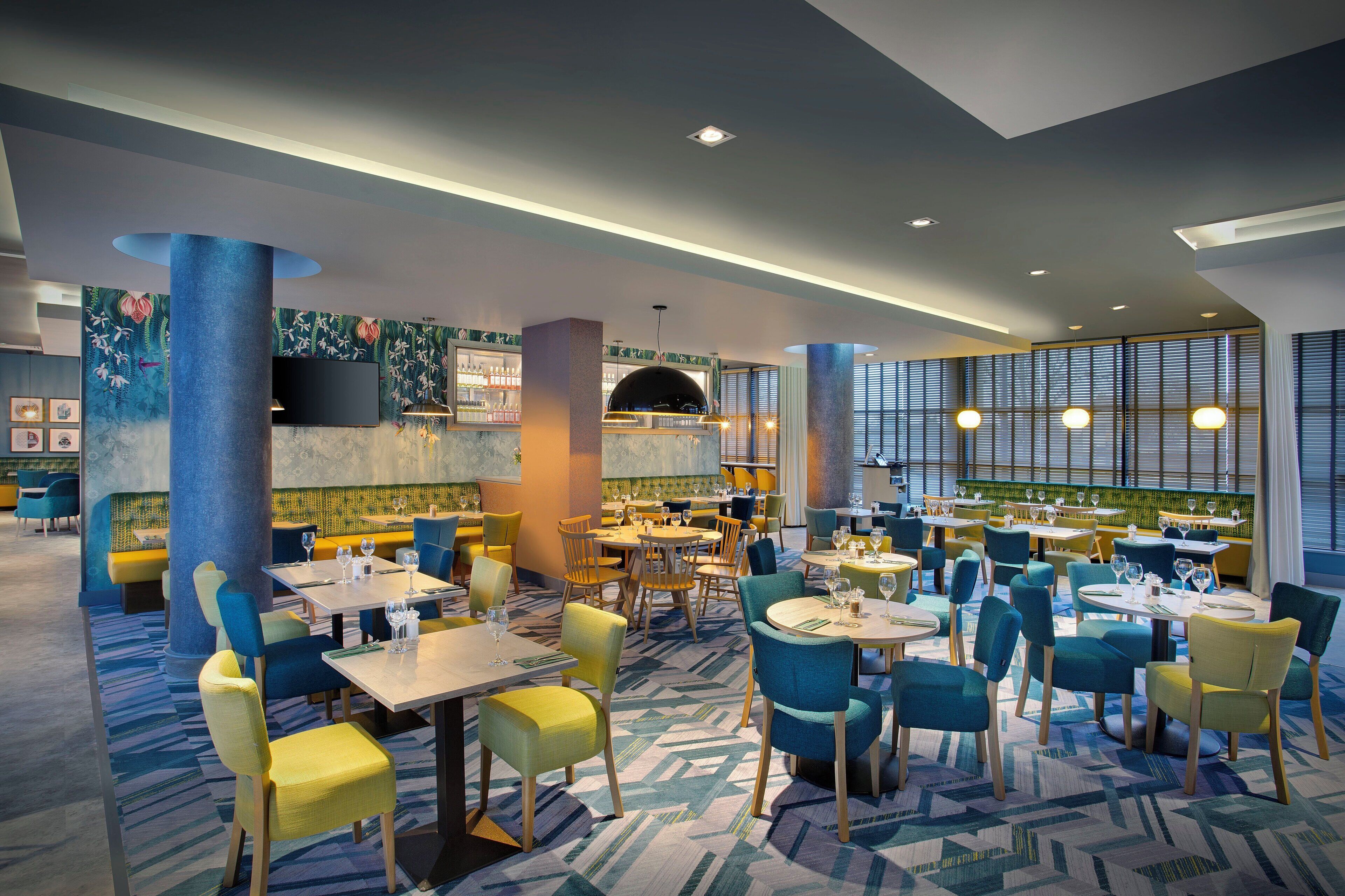 A modern restaurant interior with multiple dining areas, a bar, and a large screen.