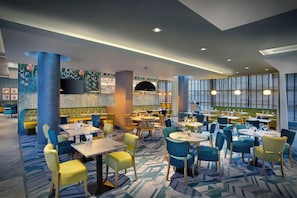 A modern restaurant interior with multiple dining areas, a bar, and a large screen.