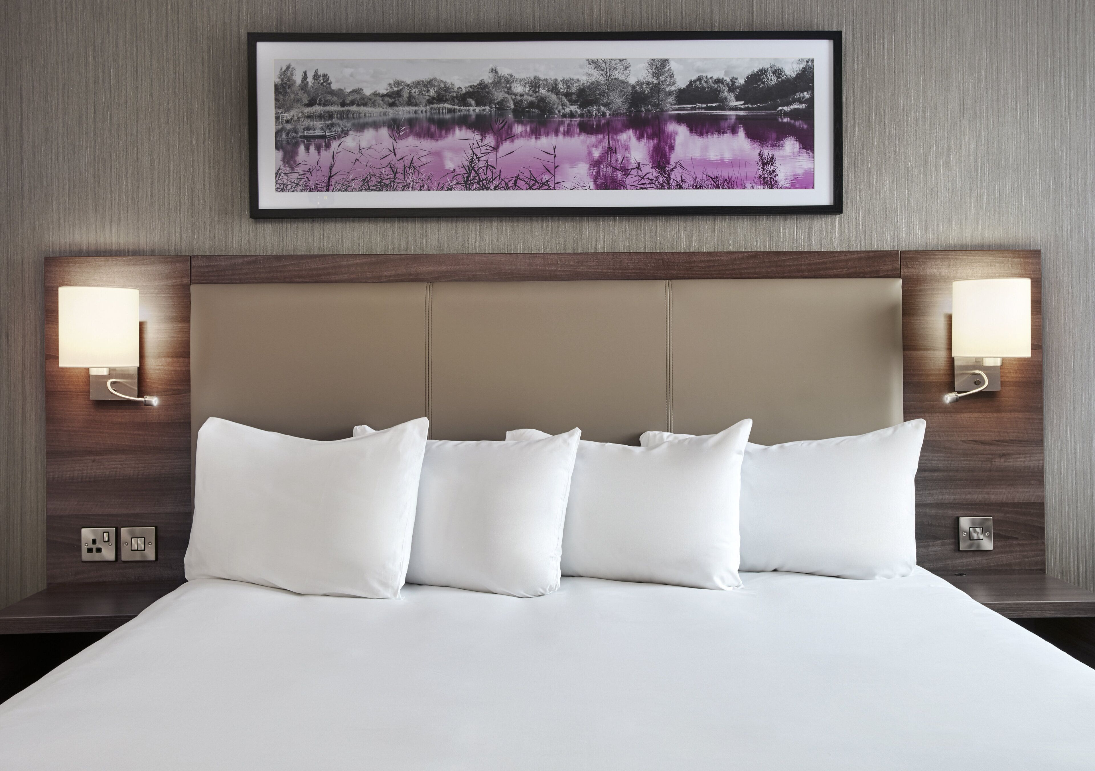 A hotel room with a large bed, two bedside lamps, and a framed picture above the bed.
