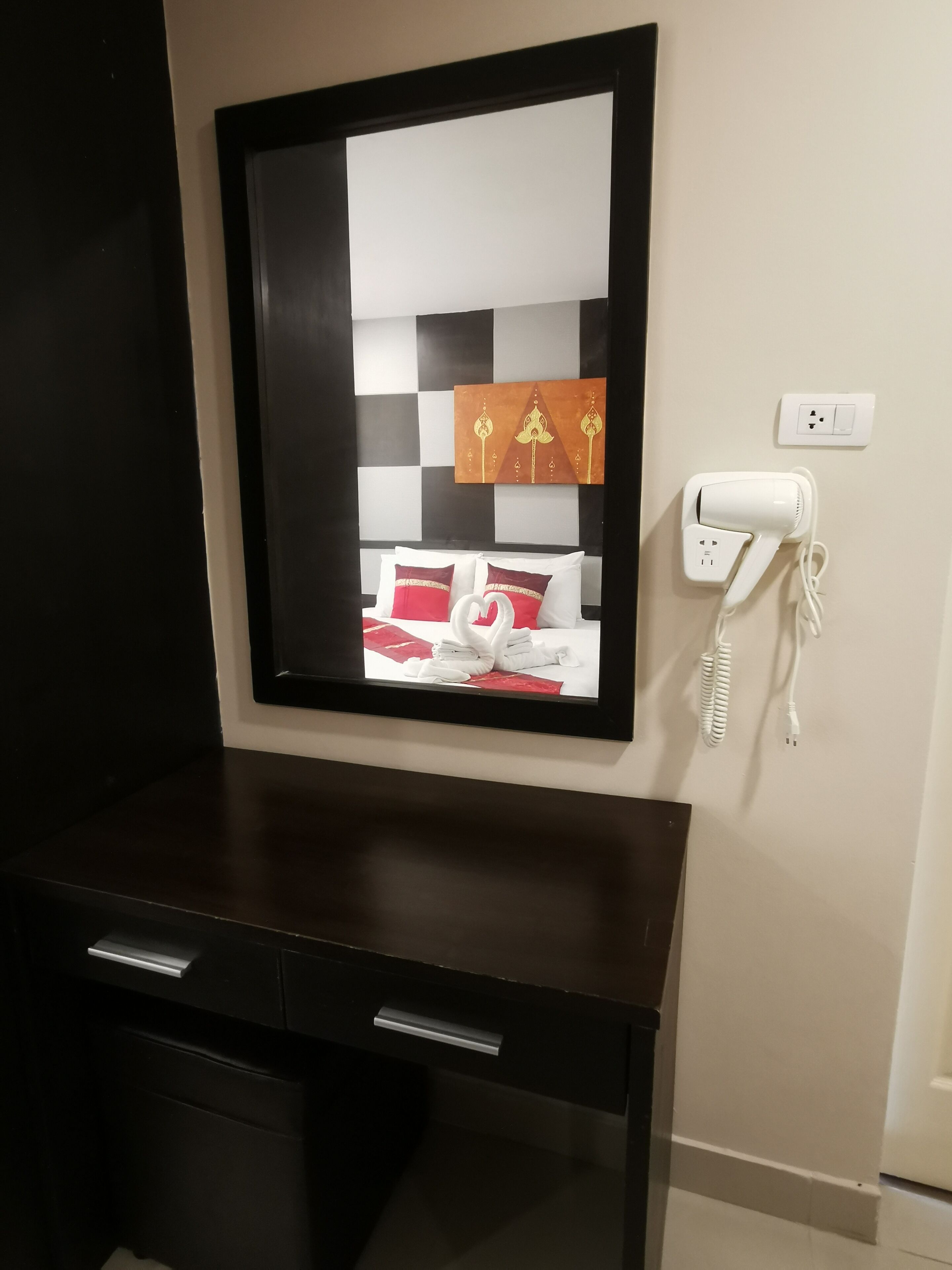 Une chambre d’hôtel avec un grand miroir, une table de chevet équipée d’un sèche-cheveux et une prise électrique au mur.