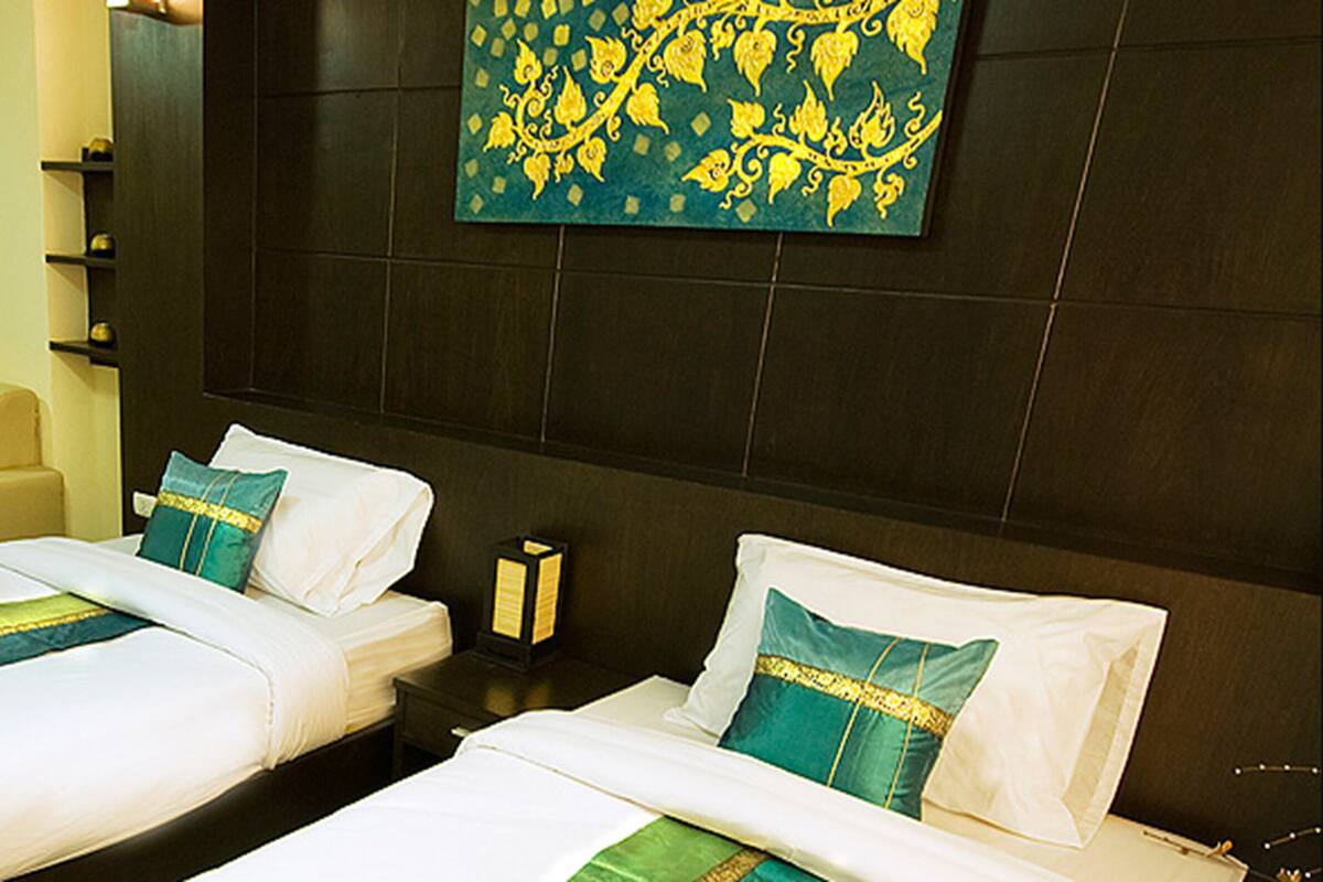 A hotel room with two beds, a desk, a chair, a small table with a plant, and a decorative wall piece.
