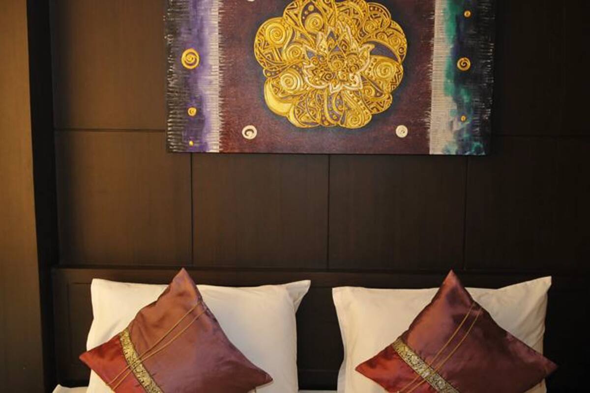A hotel room with a dark headboard, two white pillows, and two red pillows with gold trim.