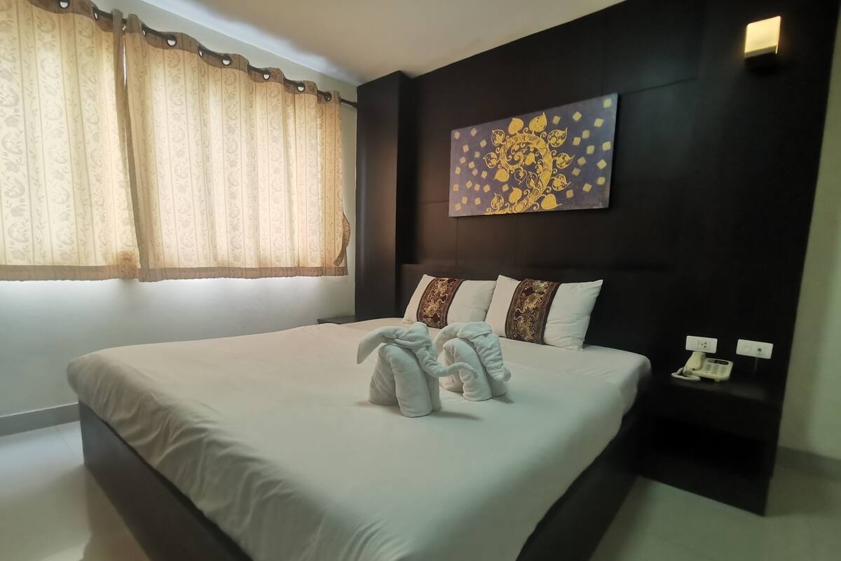 A neatly made bed with a white comforter and two towels folded at the foot.