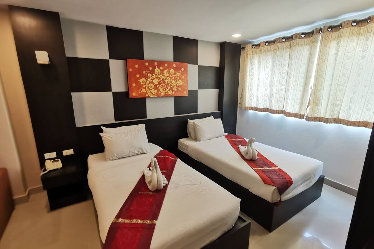 A hotel room with two beds, a checkered wall design, a decorative wall piece, and a window with curtains.
